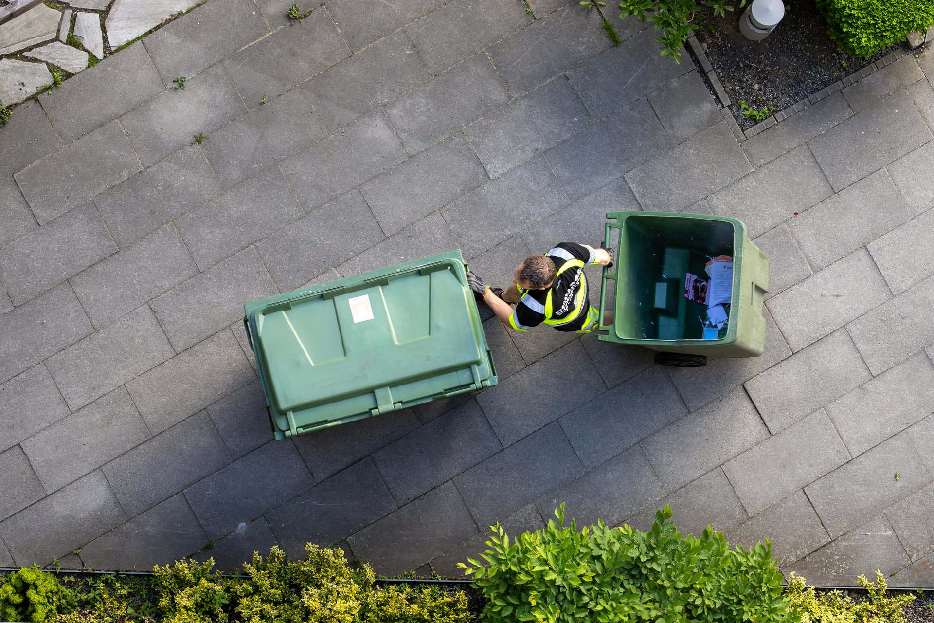 Stockholm, Sweden June 5, 2024 A garbage man in a residential complex pushes and pulls green garbage containers.