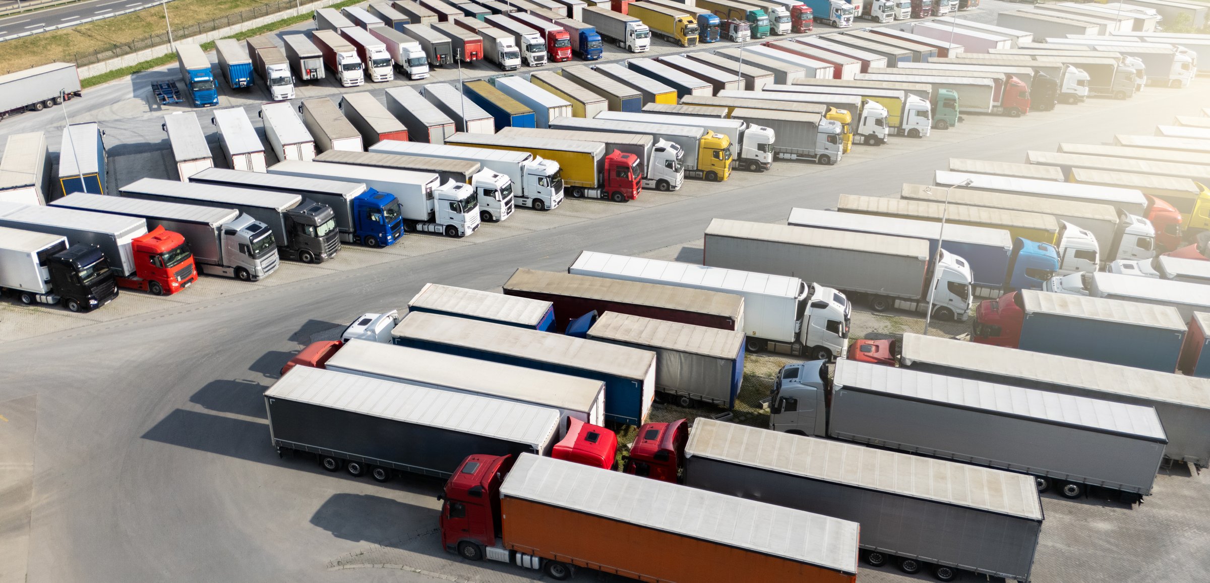 Aerial view of a large truck parking lot at a logistics hub, with multiple commercial semi trucks parked in organized rows