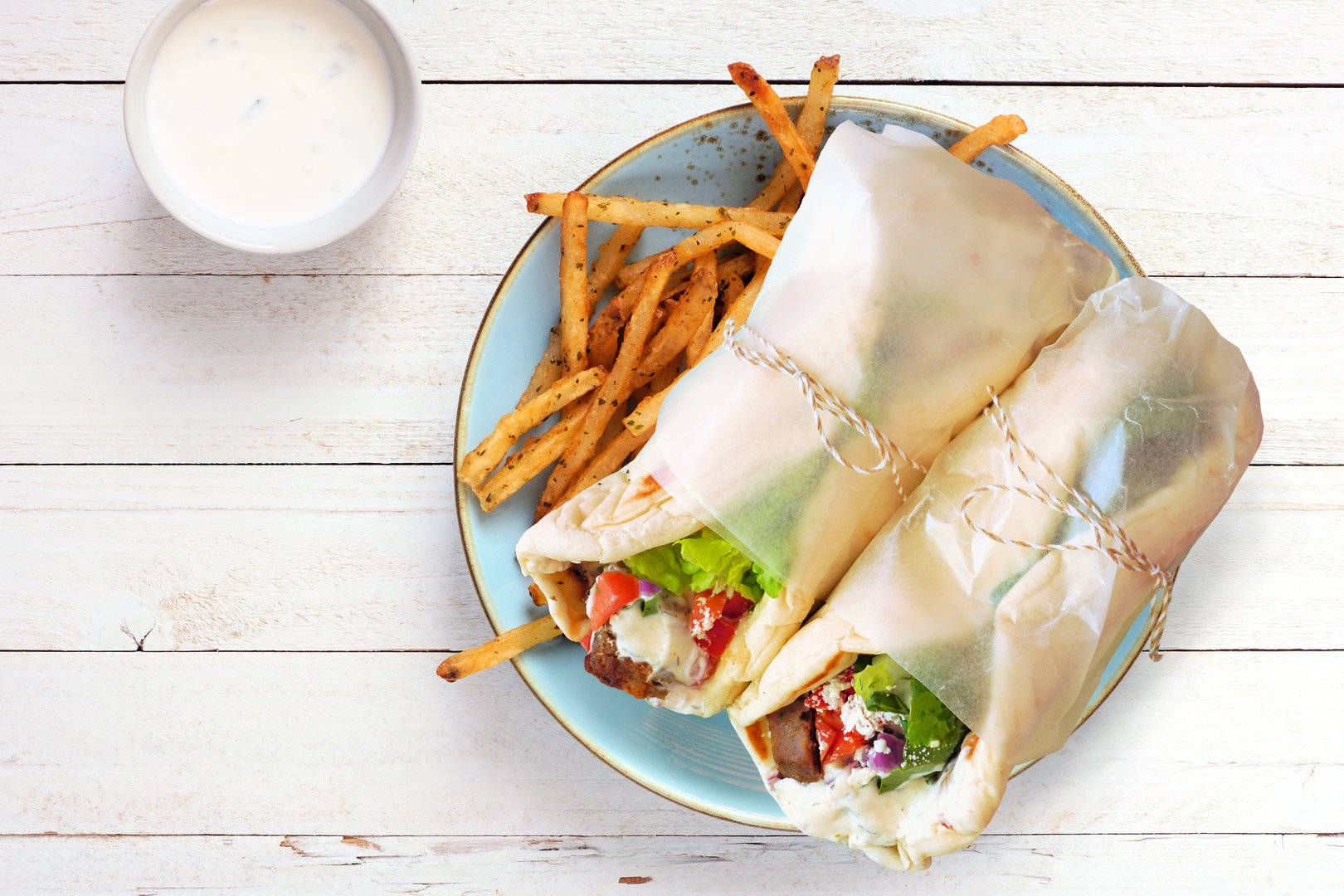 Greek gyros pita wraps with fries and tzatziki. Above view on a white wood background.