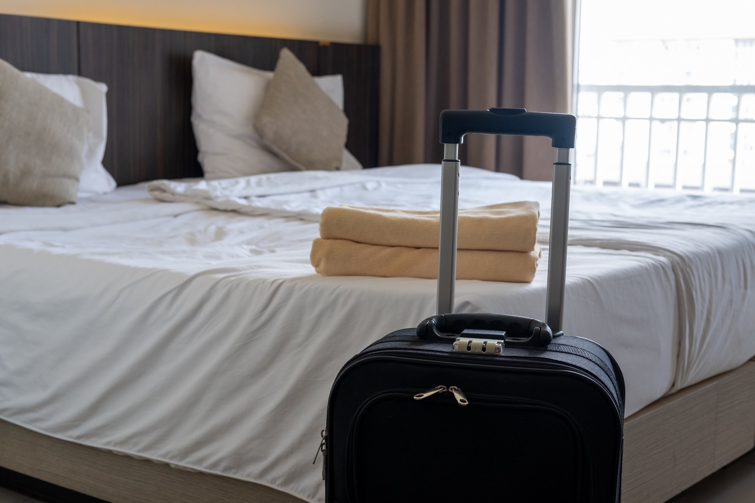 Traveler's luggage placed beside bed in cozy hotel room symbolizing vacation and relaxation stay