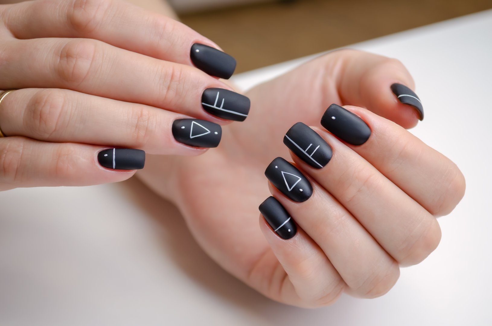 The hands of a young woman with a black matte gel polish and geometric design. Manicure Ideas