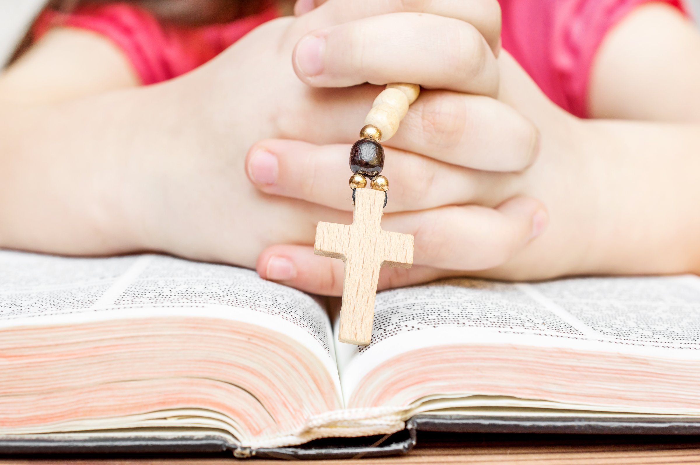 Child praying over opened Bible holding rosary.
