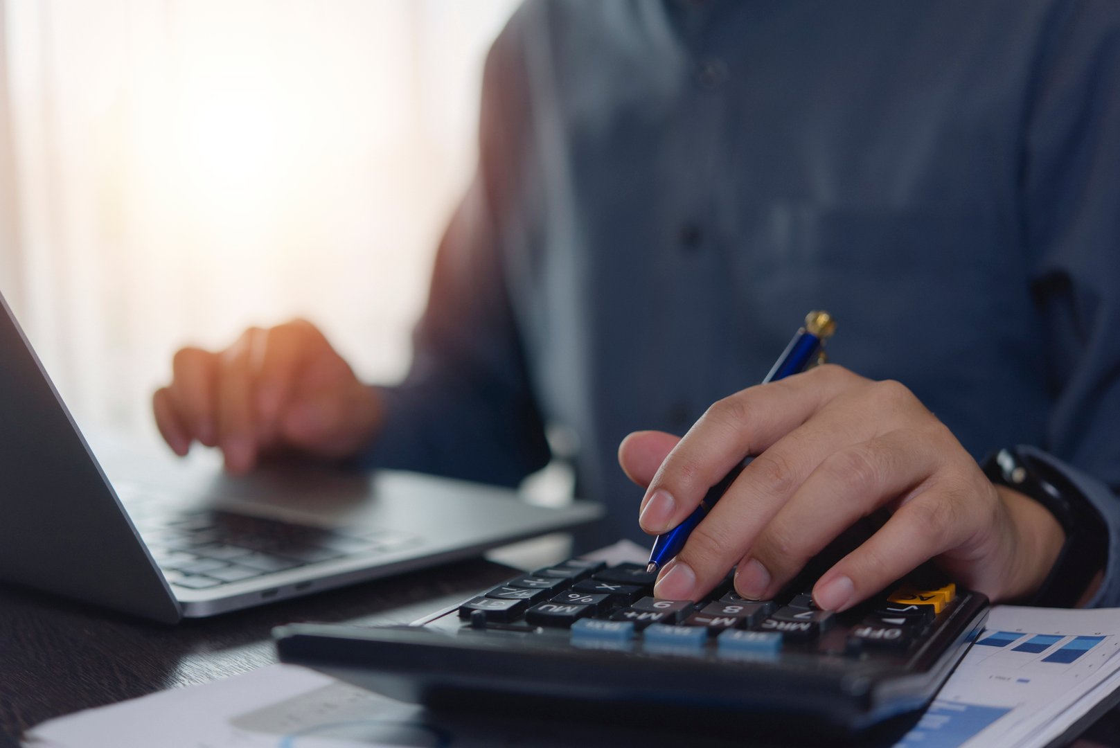 Accountant working hands using calculator and laptop. business finance planning at desk with financial tax documents invoice , pen, and technology management payroll online internet banking concept.