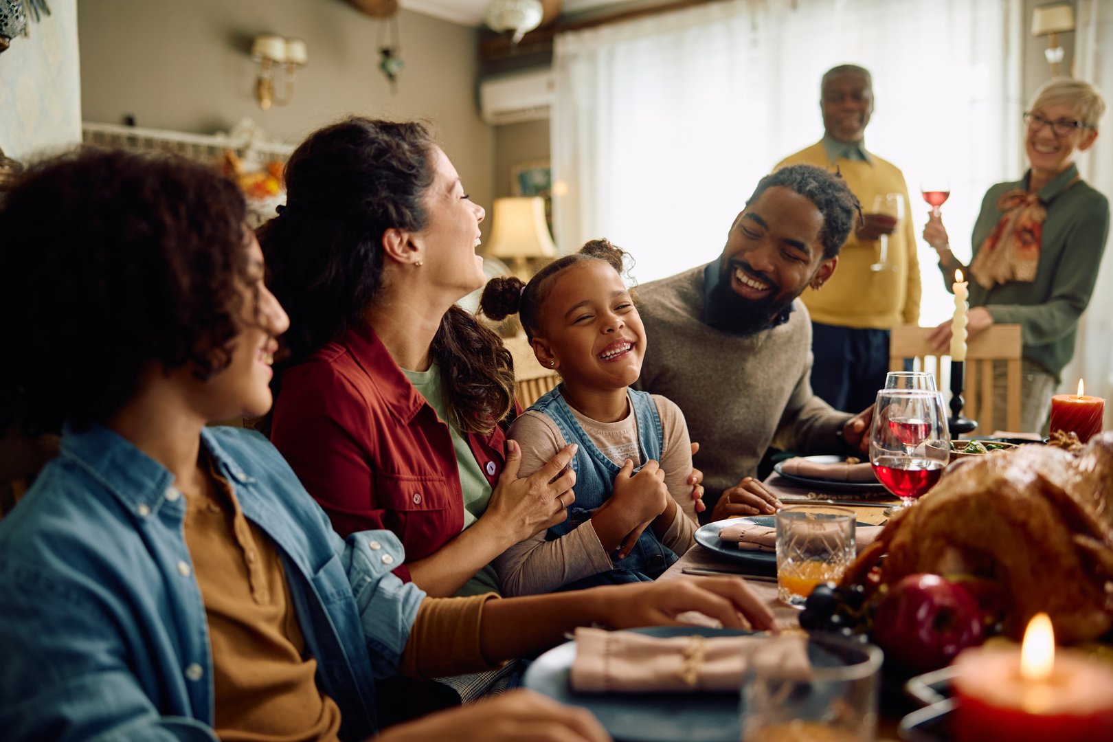 Happy African American girl laughing while enjoying in Thanksgiving dinner with her extended family in dining room.