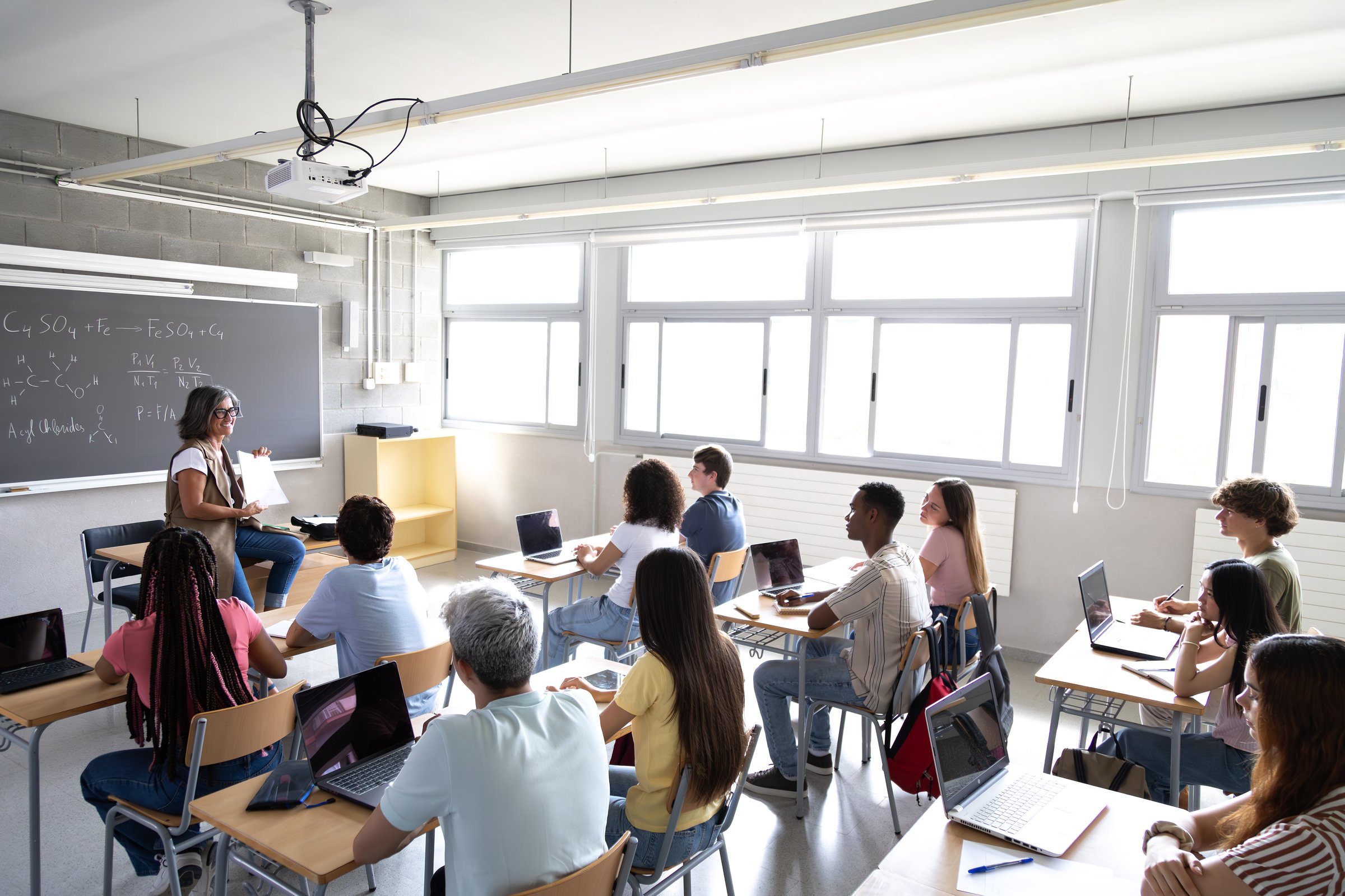 High angle view of mature female teacher explaining lesson to multiracial high school students in class. Back to school concept.