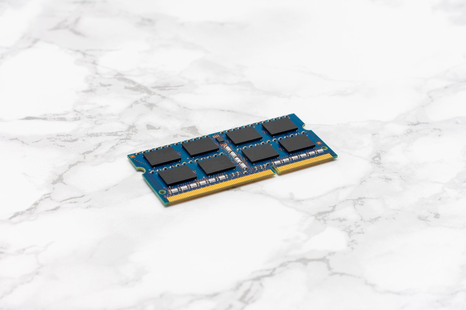 Blue computer RAM Sticks sits on a white countertop. The part is a computer memory stick, and it is laying on its side.