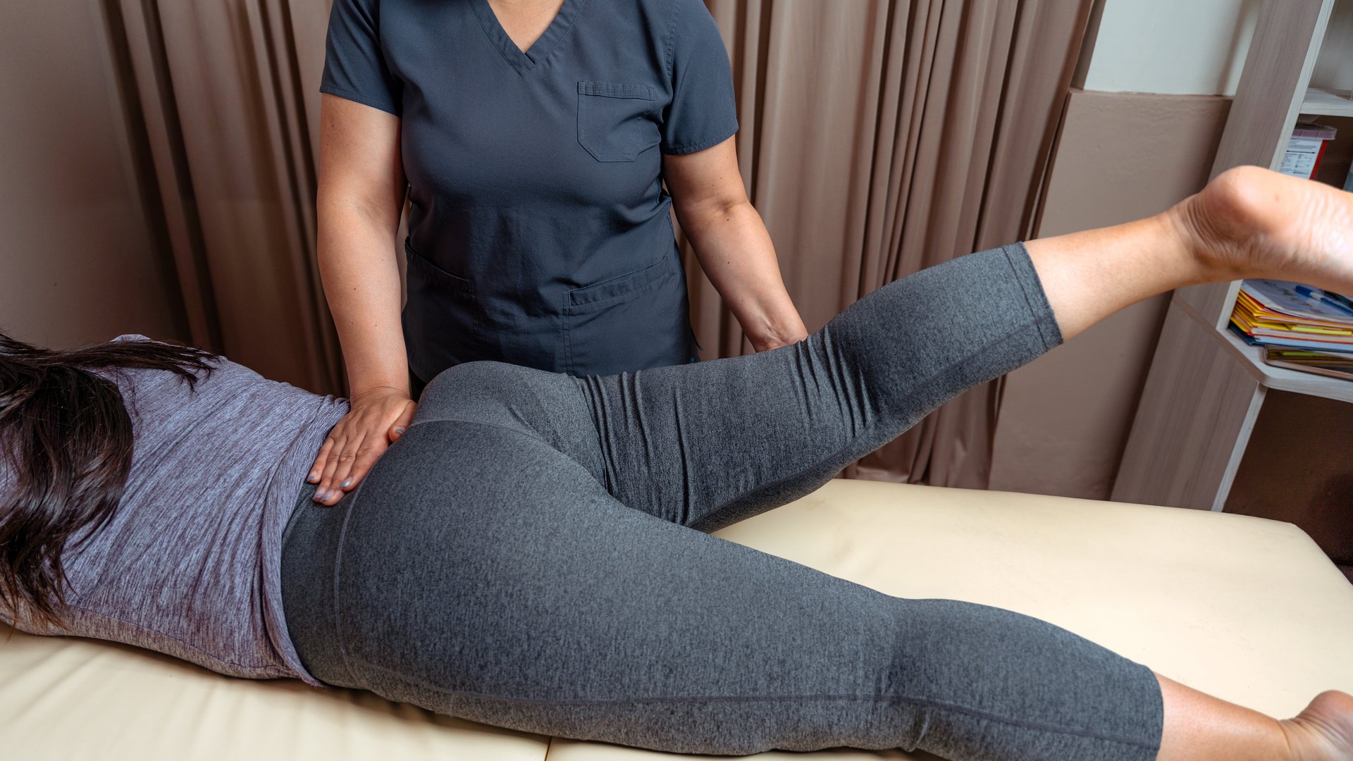 Physical therapist helping a young woman with leg and hip exercises in a clinic