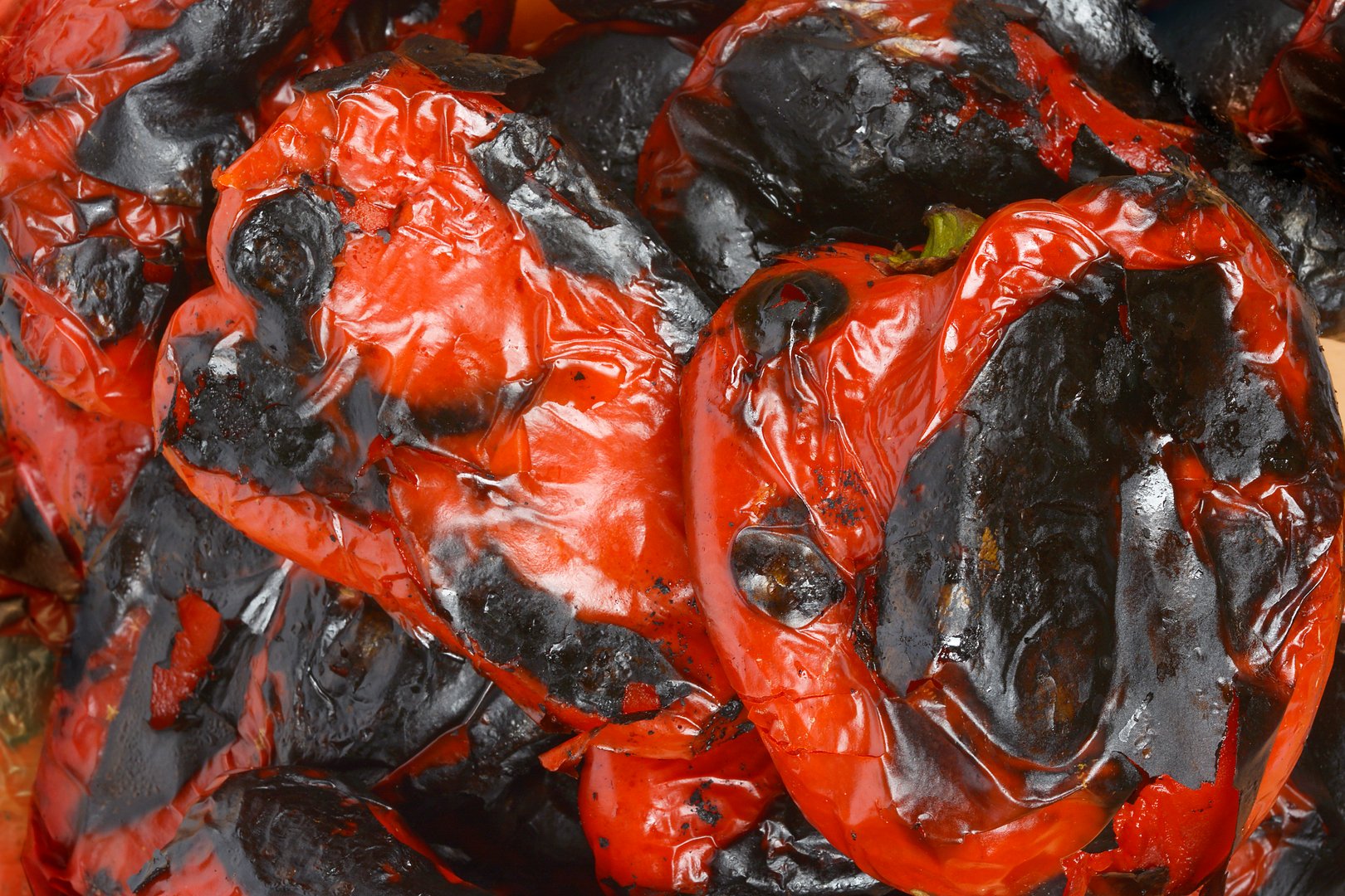 A detailed, high-angle view of a bowl of roasted red Macedonian sweet peppers, revealing the intricate texture of their wrinkled and charred skin