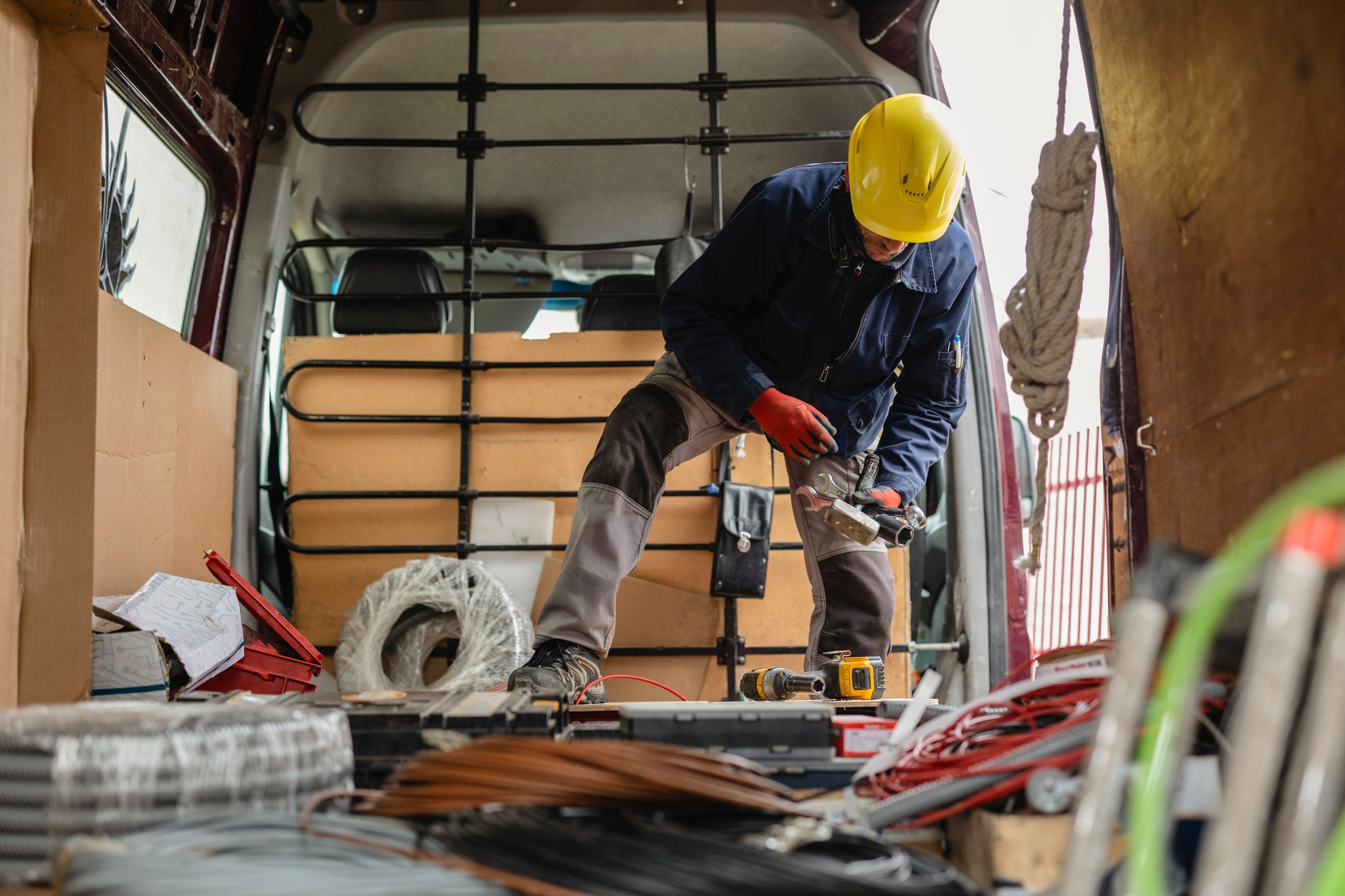 Electrician wearing protective gloves and helmet is preparing cables and equipment inside his van, getting ready for an installation job