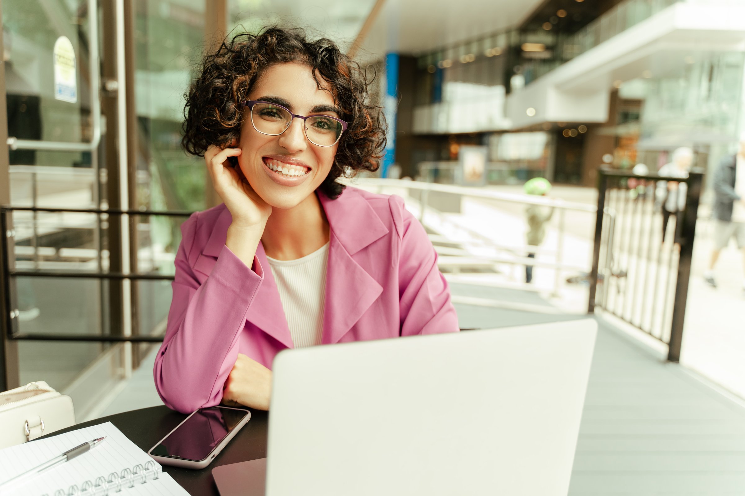 Young businesswoman is sitting at a table outside a cafe, working on her laptop and smiling