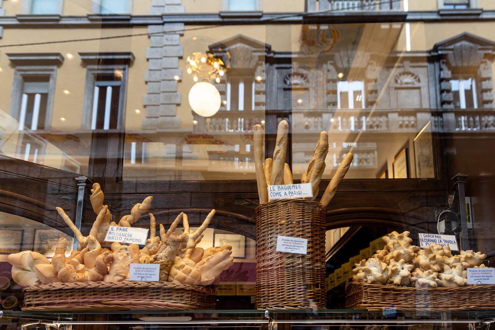 Artisanal bread display in a shop window, reflecting the city and buildings of Bologna, Italy