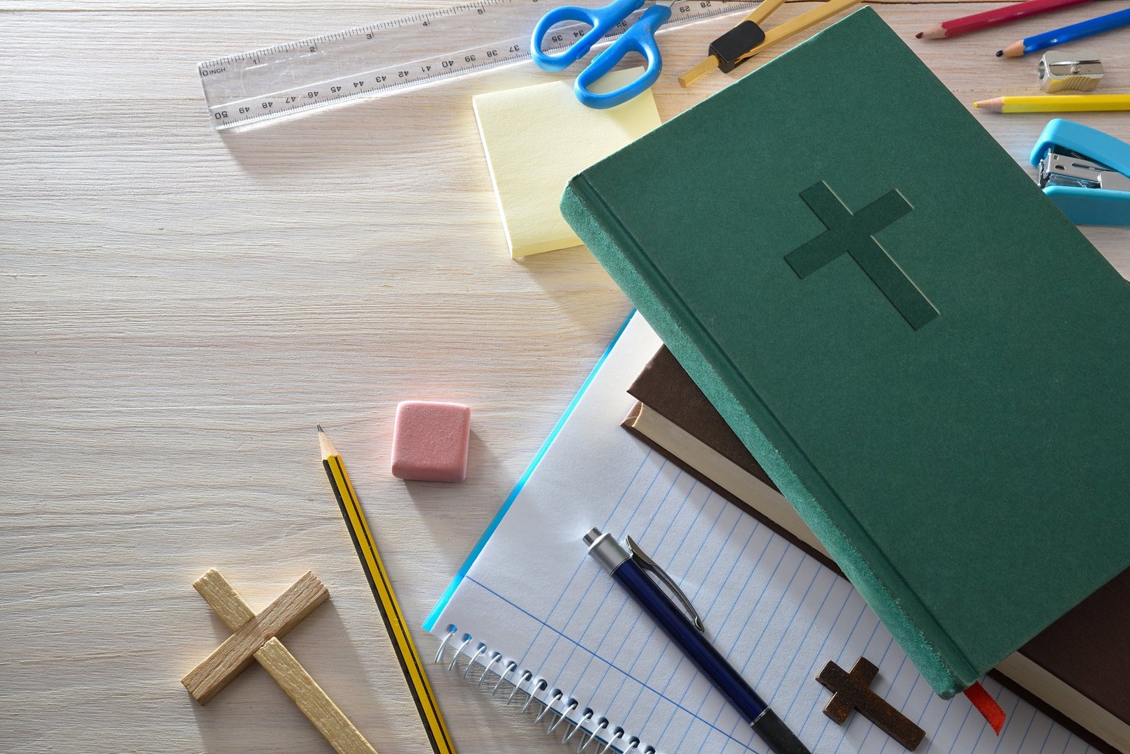 Religious educational background with school supplies on a wooden bench such as notebooks, pencils, ruler and other tools and a green Bible. Top view.