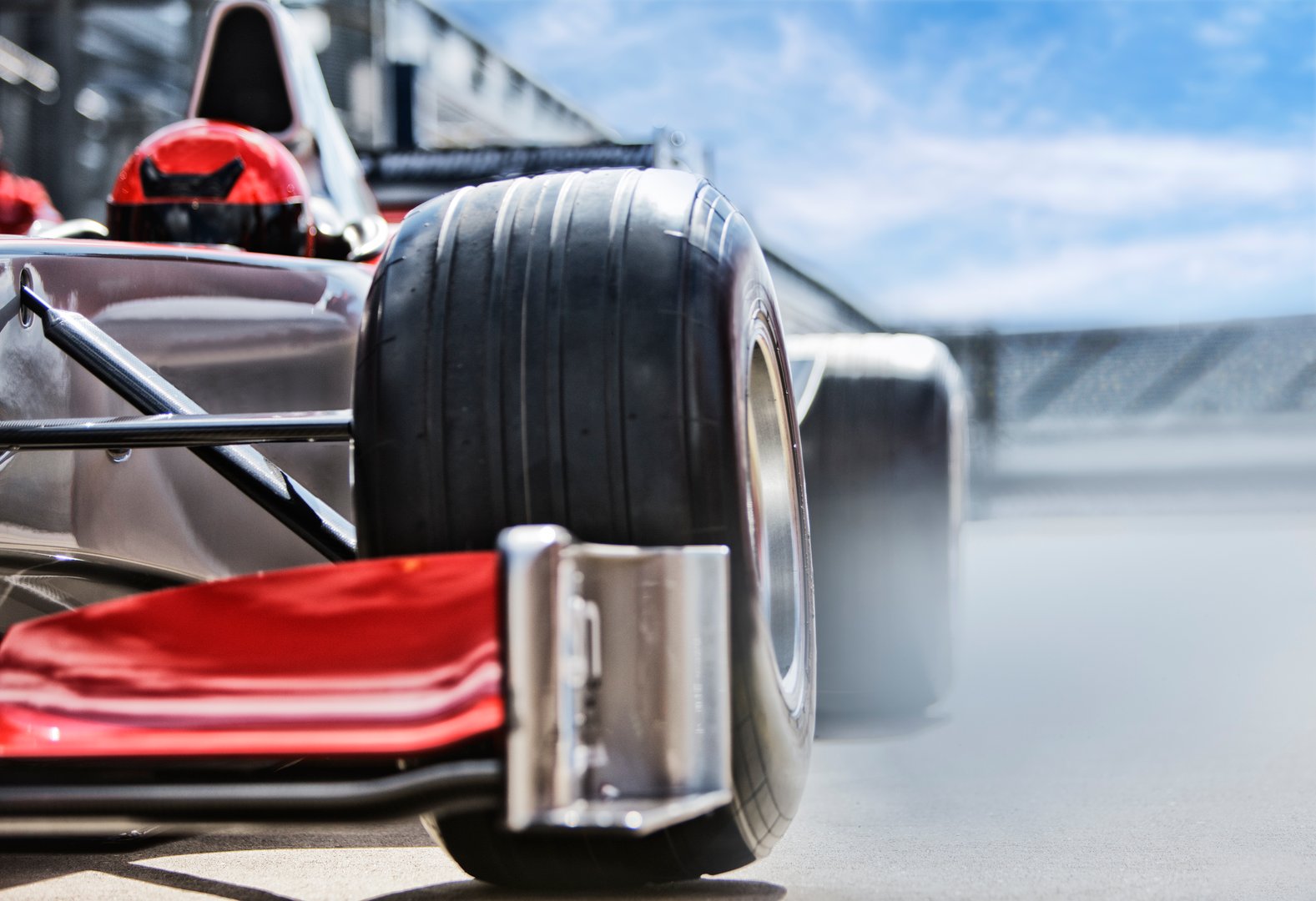 Close-up of a red Formula 1 car's rear wheel and spoiler with smoke, suggesting speed on a racetrack.