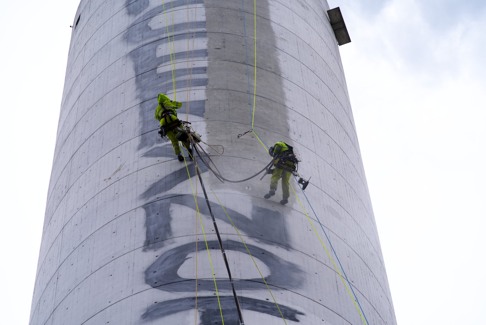 Two industrial climbers roping from chimney and cleaning graffiti vandalism with special equipment. Photo taken April 5th, 2022, Zurich, Switzerland.