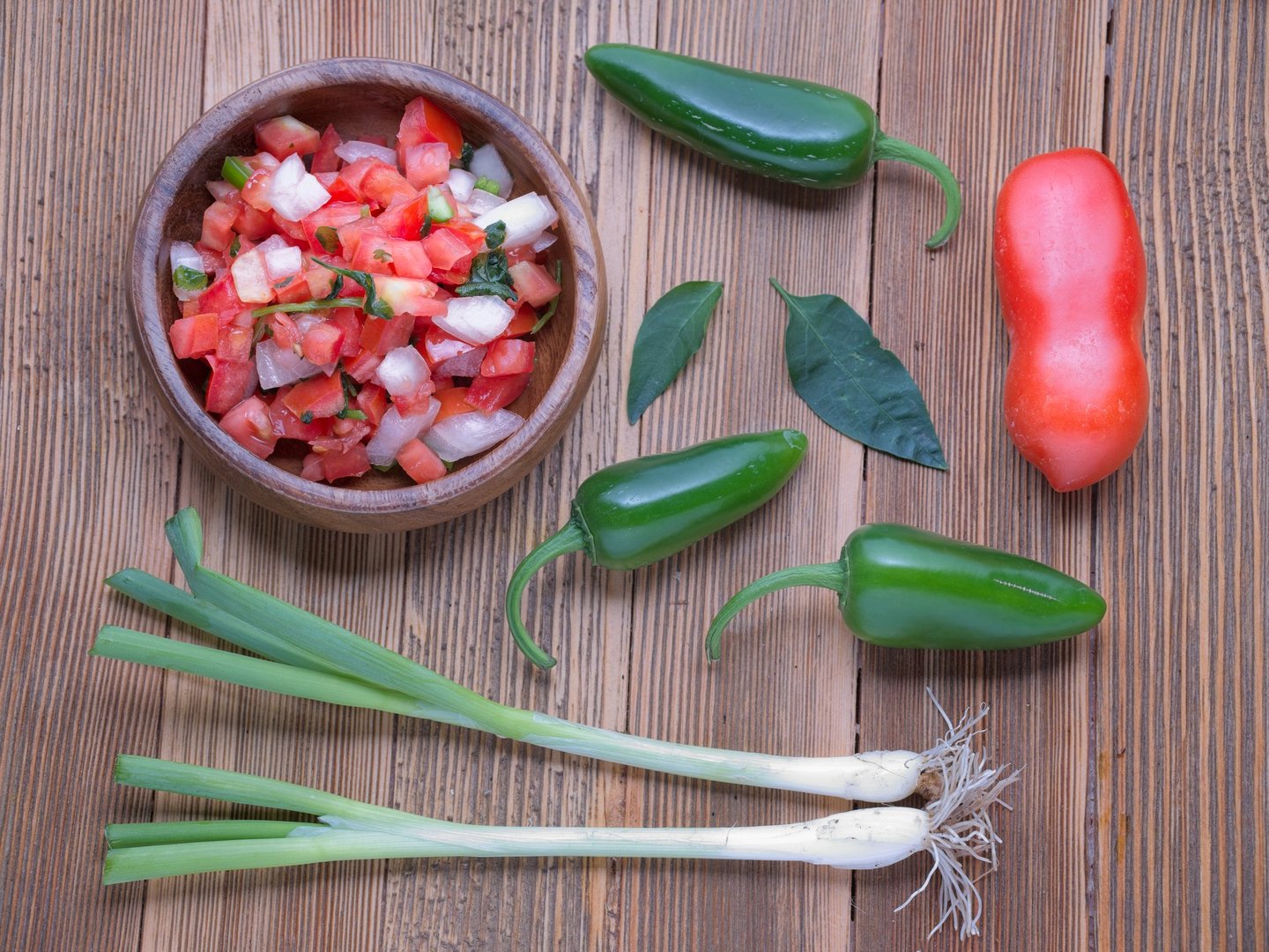 A flatlay photo of a bowl of salsa with whole tomatoes, peppers, and green onions.