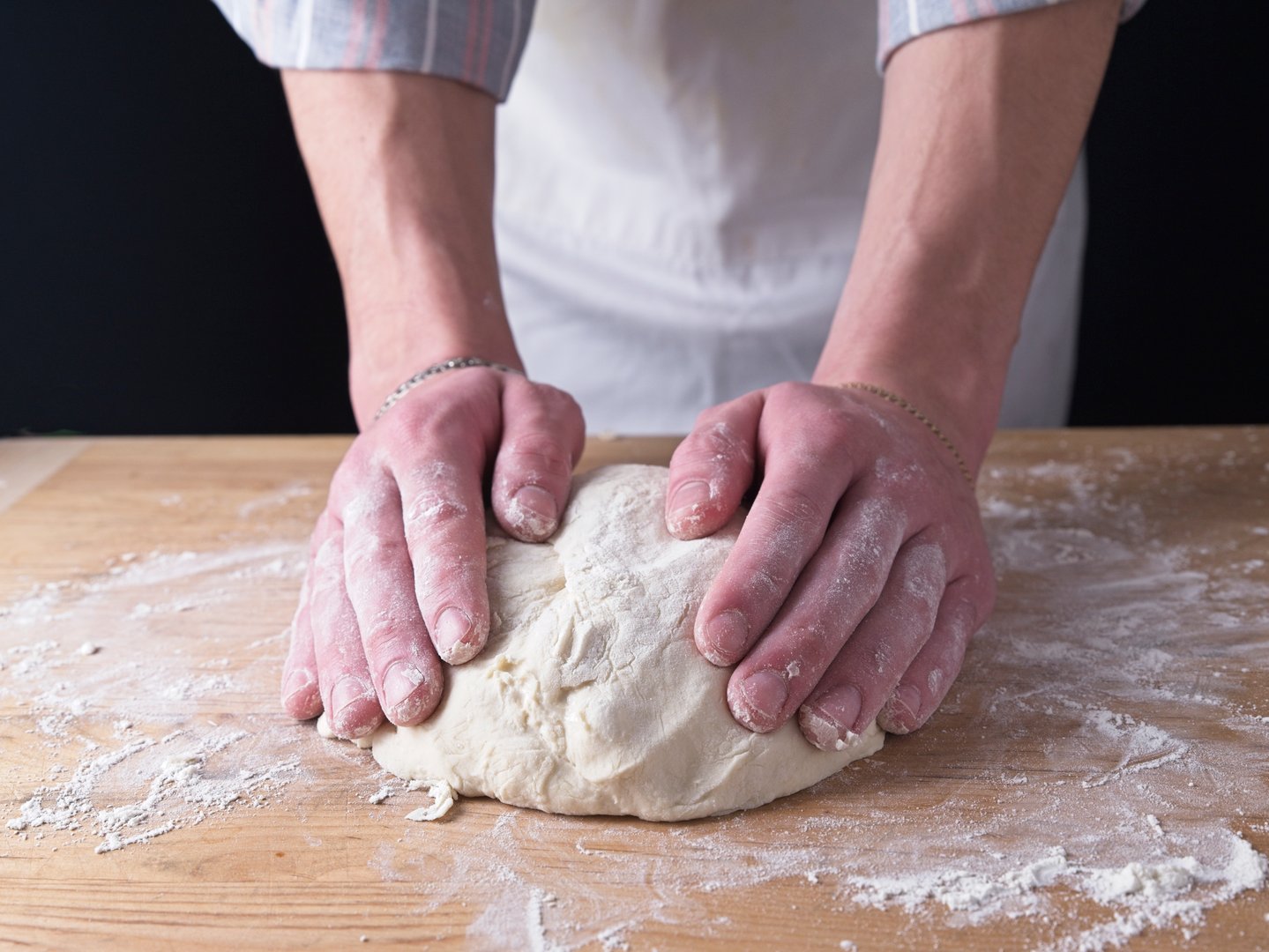 Hands forming dough into a ball on wooden table