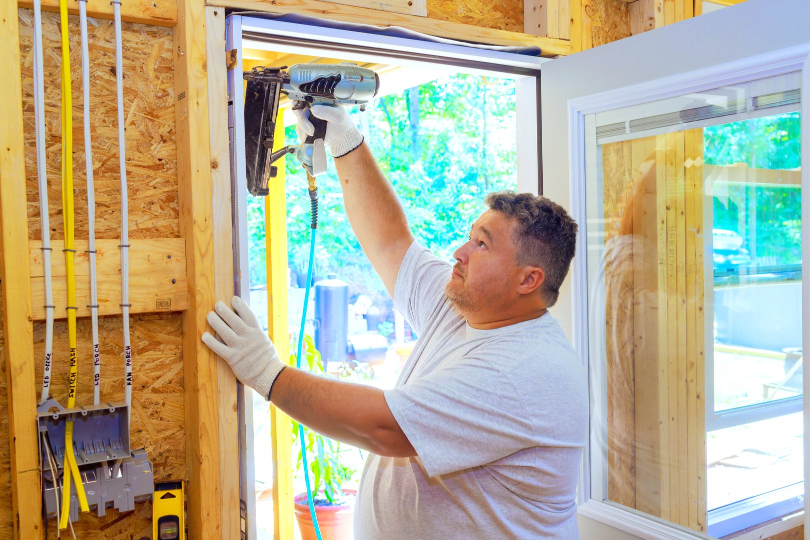 Carpenter is using pneumatic nail gun to install new front door for new house