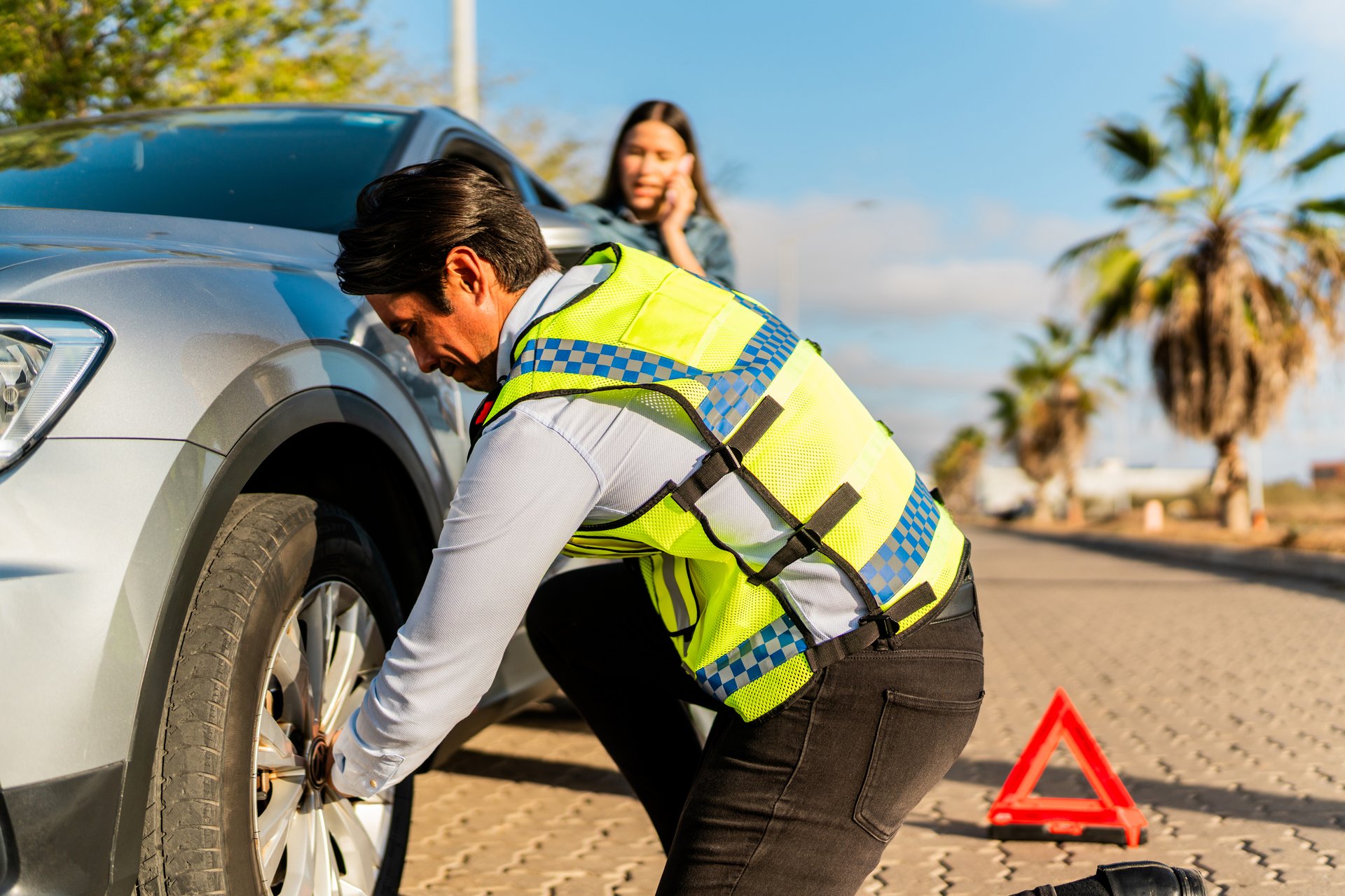 Car insurance agent changing customer's flat tire at road