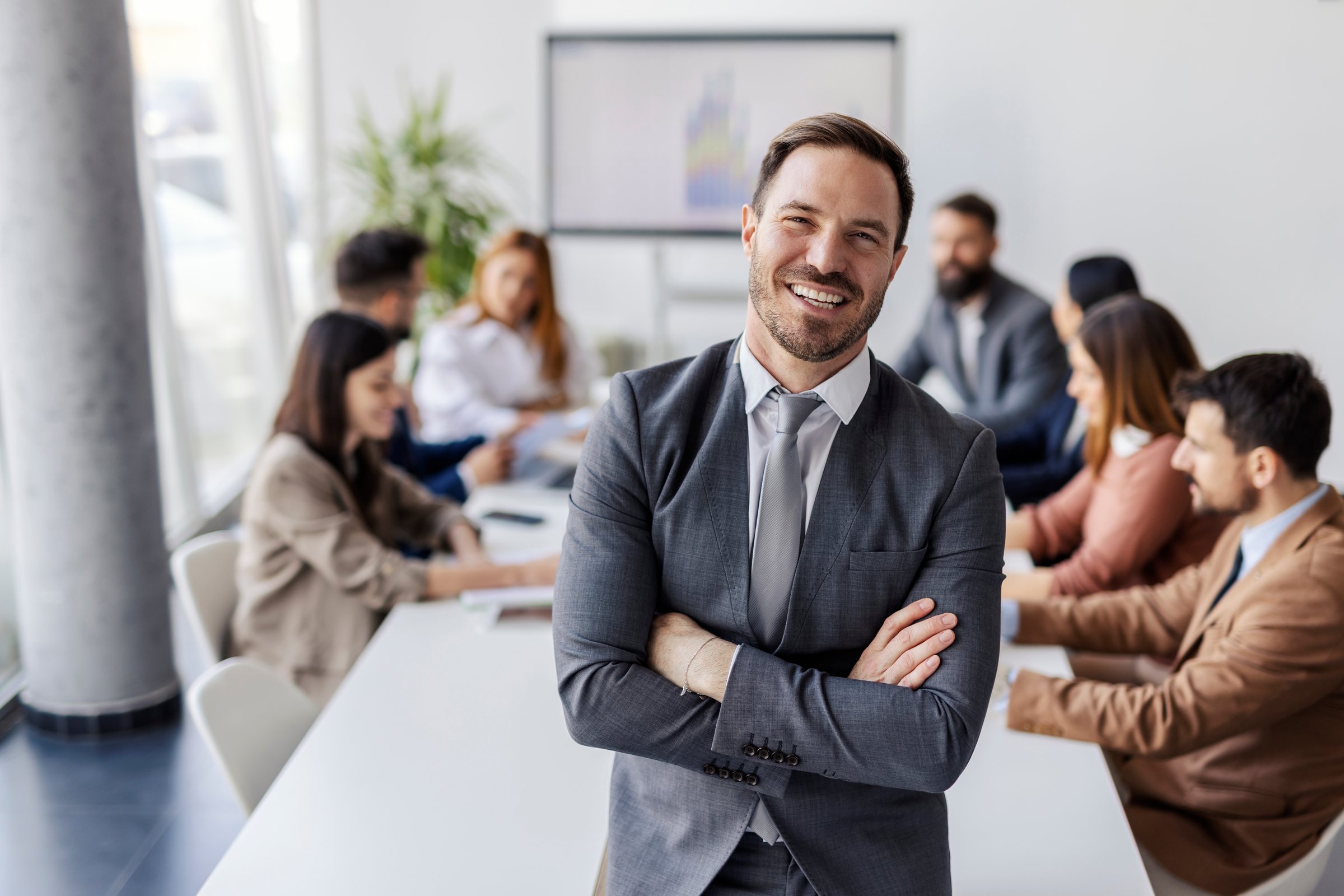 White collar worker standing at corporate office with arms crossed during the meeting and smiling at camera.