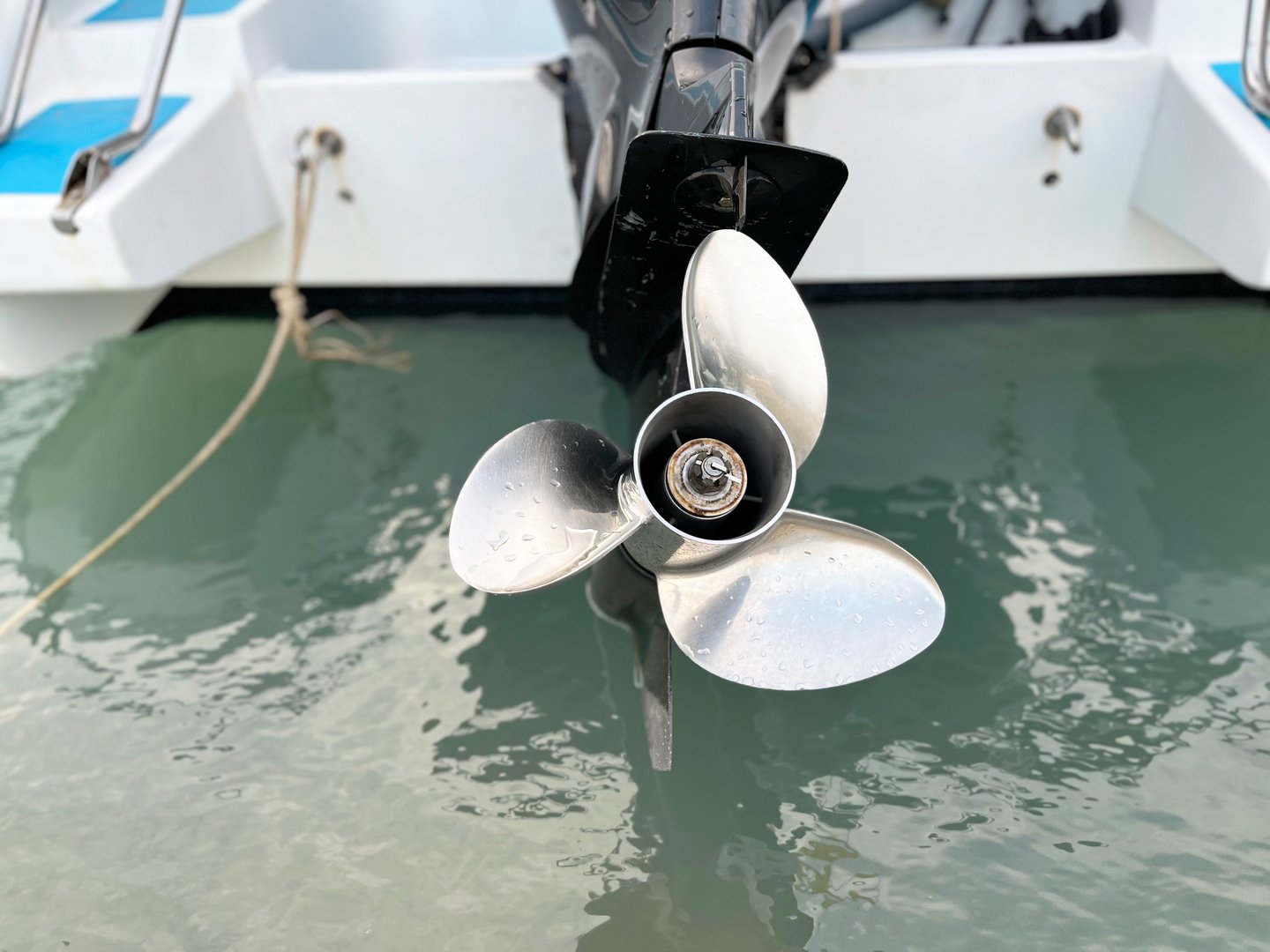bow of a boat, Close up of a shiny boat propeller attached to an outboard motor, reflecting light on the water surface. The image highlights marine engineering, watercraft components, and boating tech