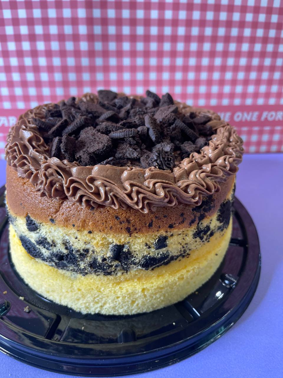 Layered cake with chocolate frosting and crushed cookies on top, set on a checkered background.