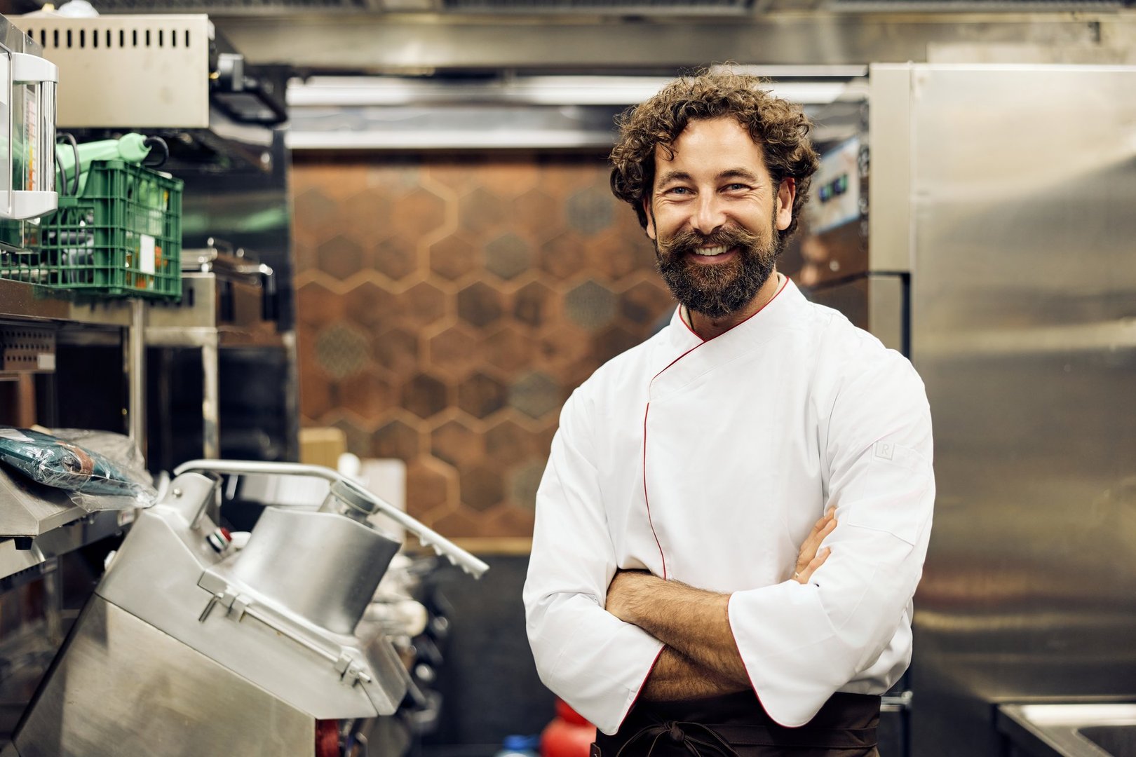 Smiling chef in a modern kitchen with confident pose and stylish uniform.