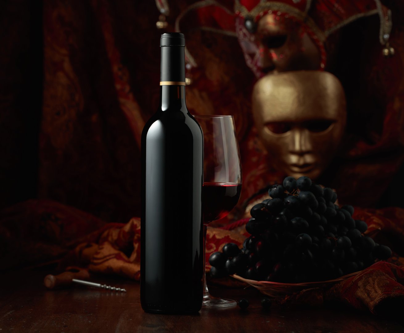 Still life with red wine, grapes, and vintage carnival masks.