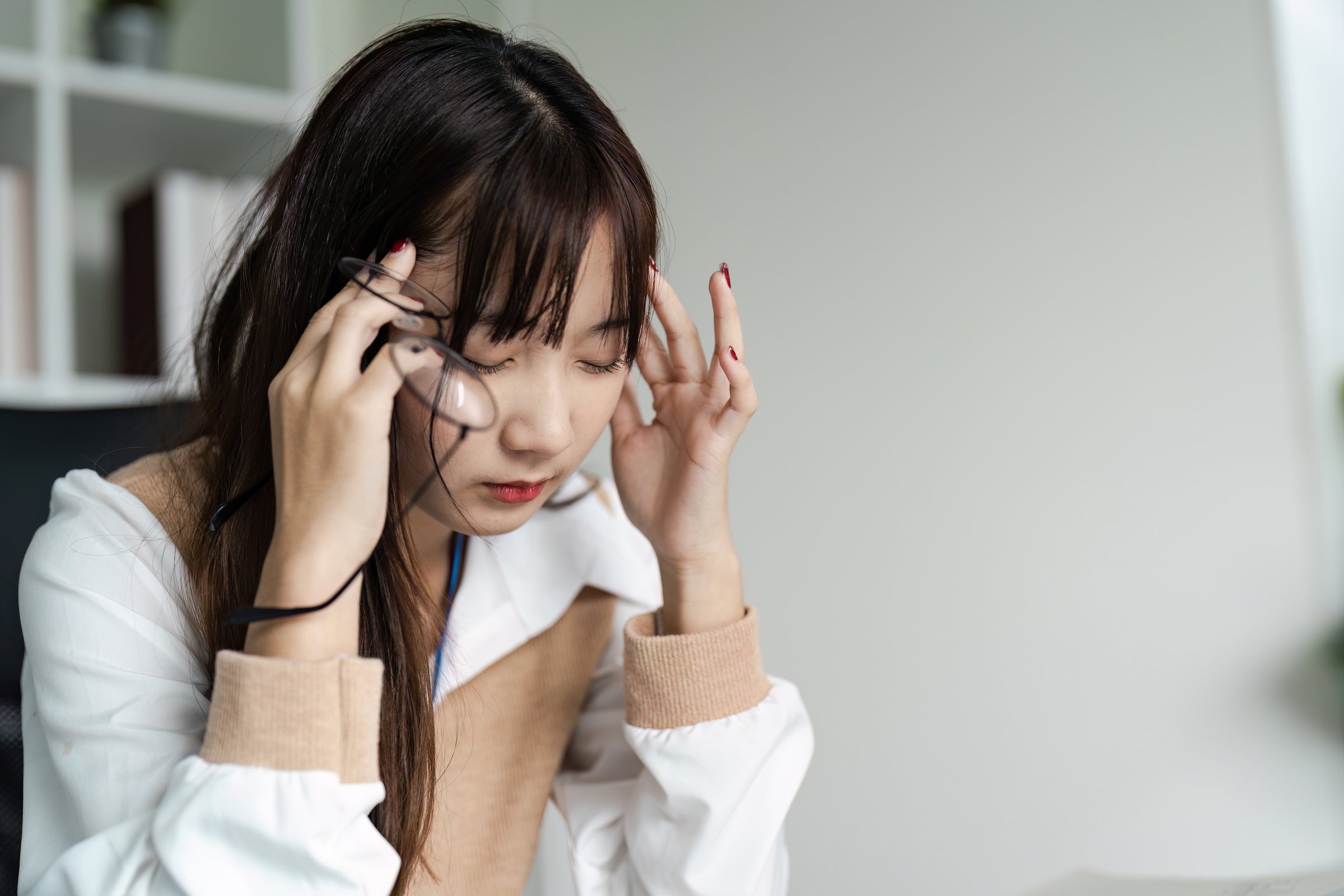 A young office worker experiencing stress and headache, indicative of office syndrome, in a modern workplace setting.