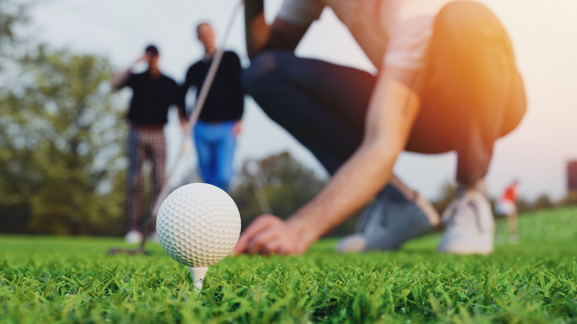 A man is placing a golf ball on a tee on a golf course. His right hand holds a golf club. His left hand is placing a golf ball on the tee. 3d, rendering, illustration,