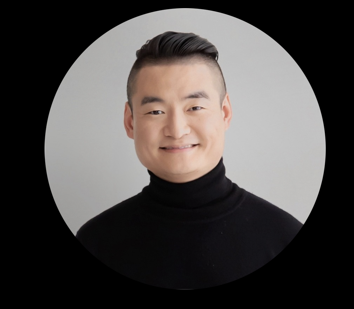 A person with short hair wearing a black turtleneck, smiling at the camera against a gray background.