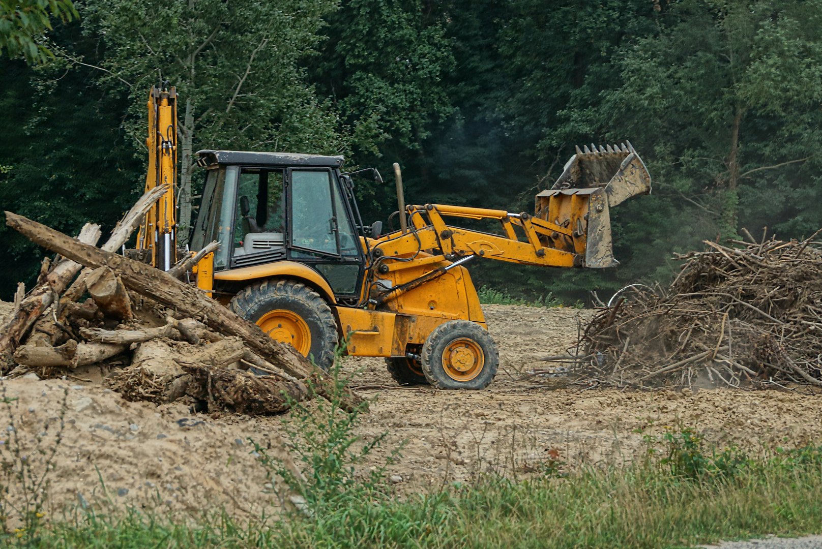 one old brown excavator with a bucket stands outside in the dry vegetation and gray earth