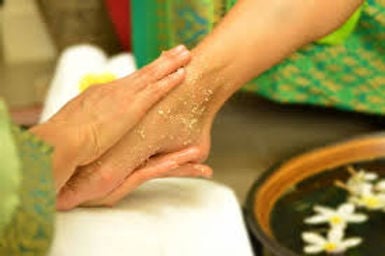 A person receiving a hand massage with an exfoliating scrub, surrounded by a relaxing spa setting with flowers.