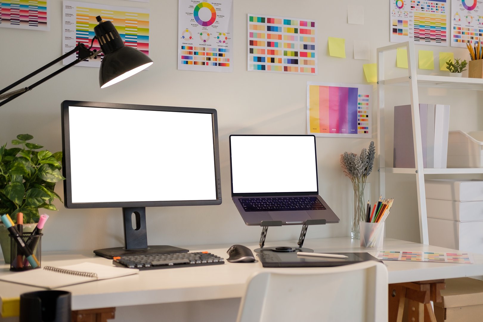 Computer monitors with blank screens on desk surrounded by color swatches and stationery in a bright design studio.