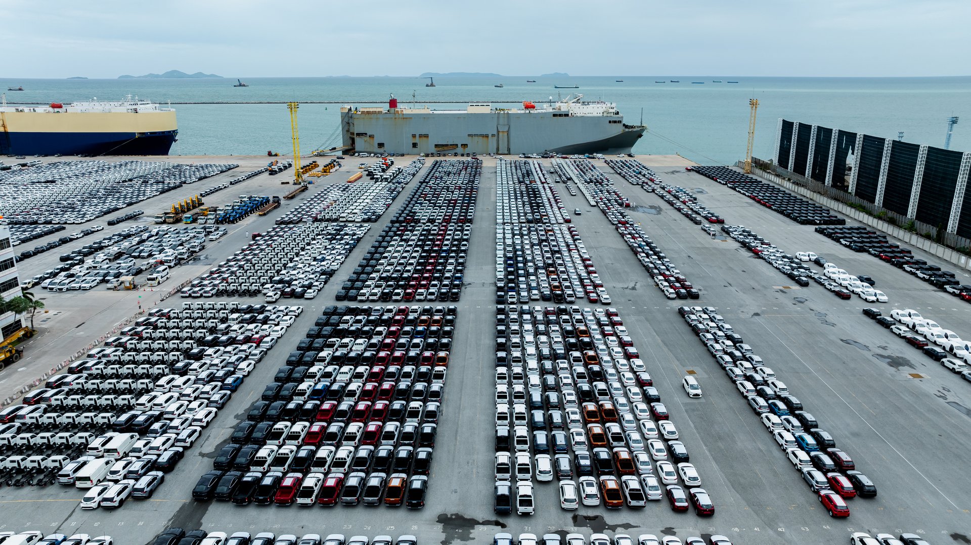 Aerial view new cars lined up in the factory and commercial port for import and export international by container ship transport  in open sea, drone point of view
