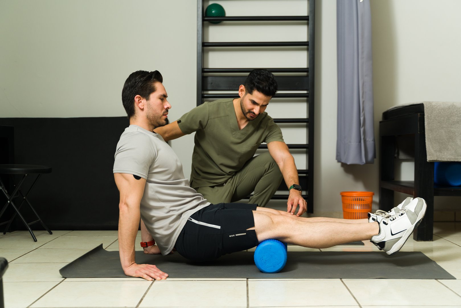 Male patient receiving leg foam rolling therapy with physiotherapist guidance, supporting muscle recovery and flexibility rehabilitation