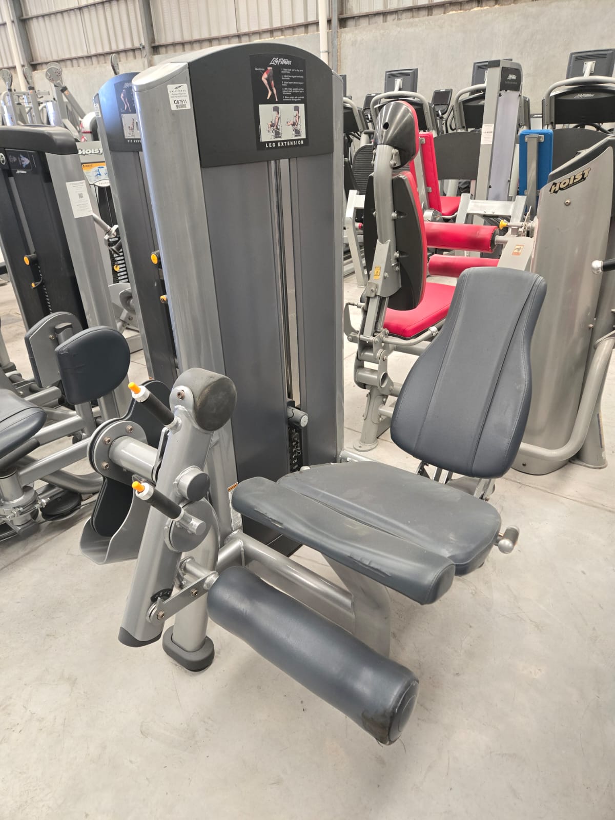 Leg exercise machine in a gym with padded seat and adjustable settings, surrounded by other fitness equipment.