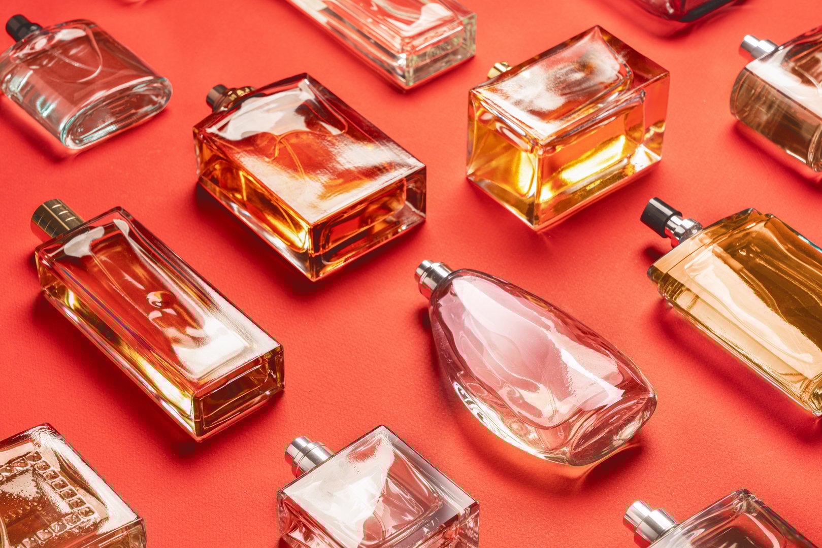 A captivating display showcases various elegant perfume bottles arranged on a striking red background. Each bottle reflects light beautifully, highlighting its unique design and color. The diverse shapes and sizes reveal the artistry behind fragrance creation, while their glossy surfaces enhance the luxurious appeal. This collection invites viewers to appreciate the beauty of cosmetics and the aromatic experiences they offer.