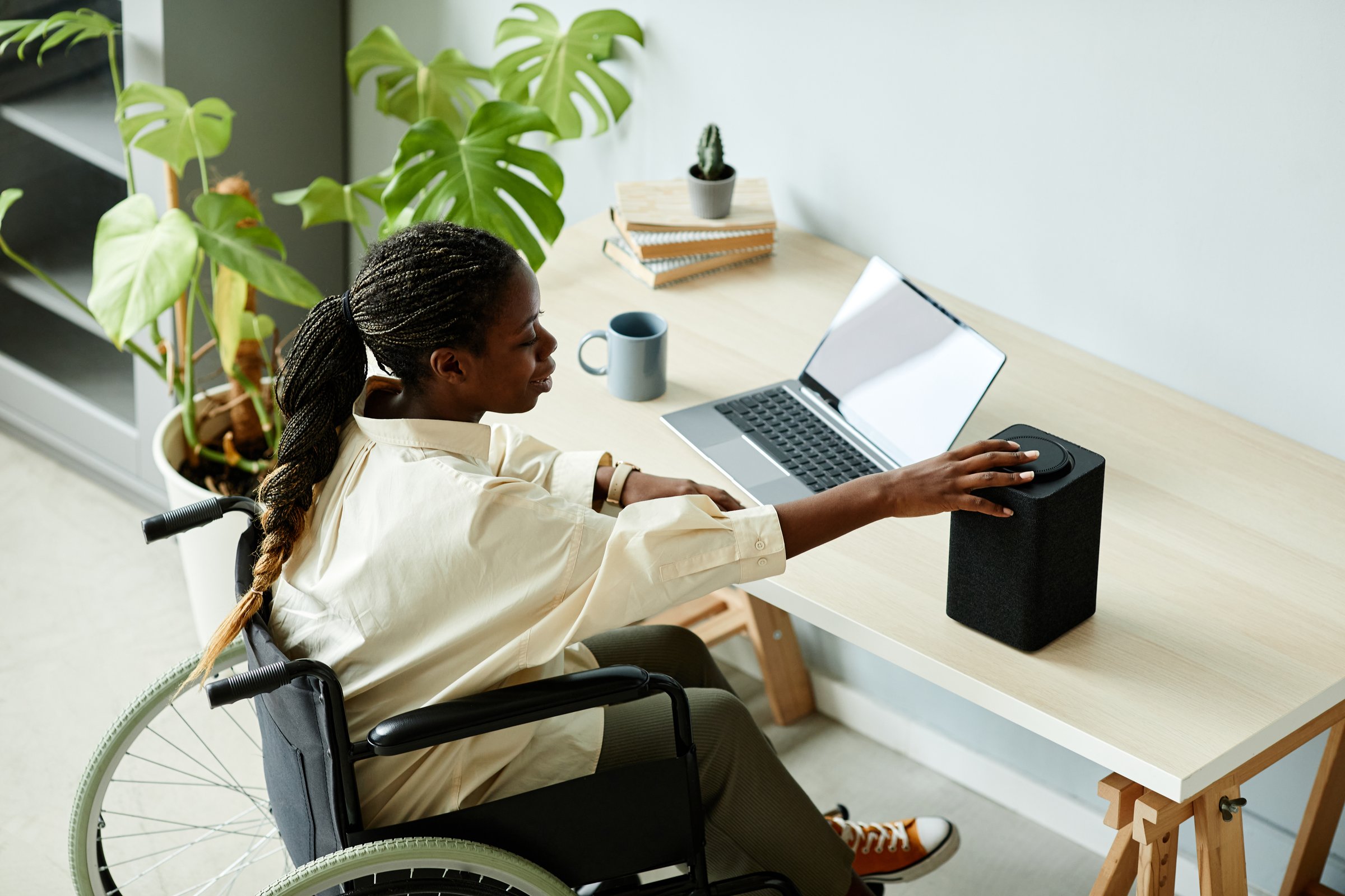 Portrait of African American woman in wheelchair using laptop while working at home office with accessible smart devices