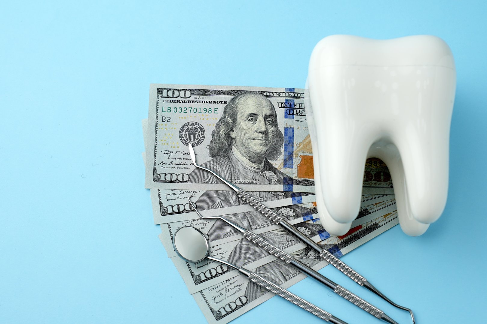 Dental Service, Insurance and dentist bill cost. The concept of saving money for dental treatment. Dollar money bills and tooth model on a bluebackgound with copy space