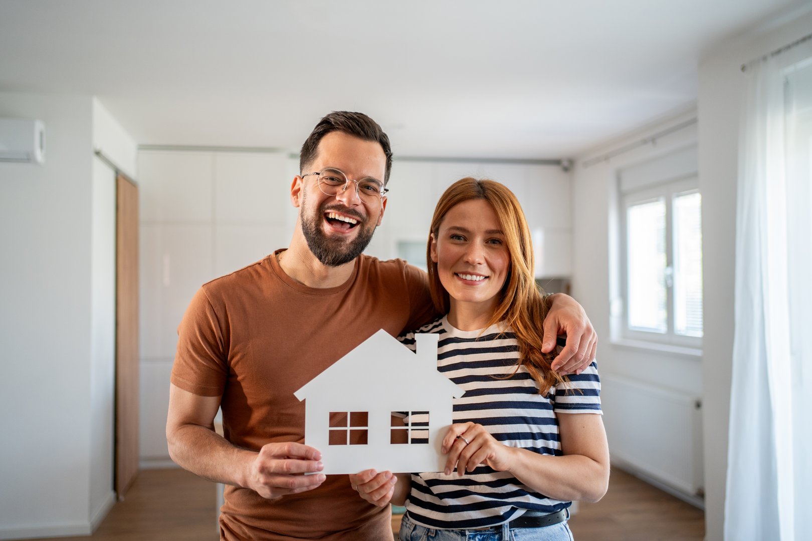 Young couple smiling while holding a white paper house