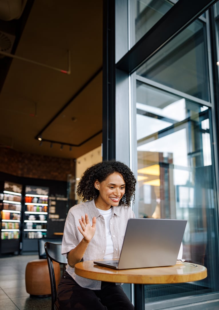 A vibrant young woman enjoys a lively video call while diligently working on her laptop in a stylish cafe setting
