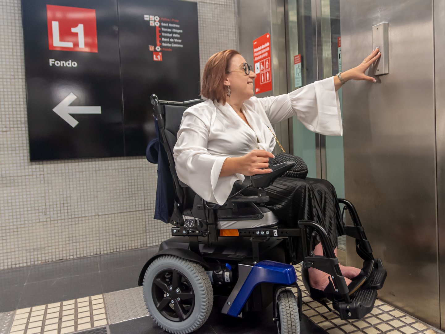 Female wheelchair user presses the button to call the elevator in the metro station, showcasing accessible design.