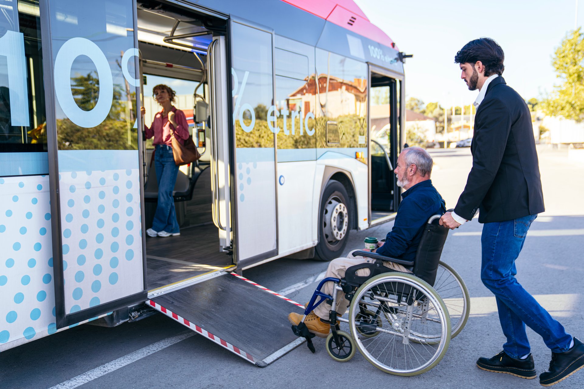 Young adult man helping a senior adult in a wheelchair using the bus ramp for public transport accessibility