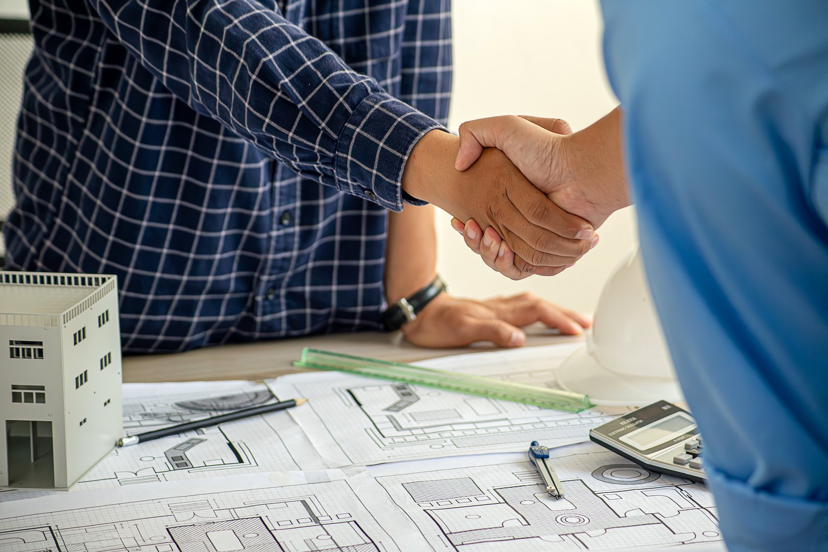 Construction engineer handshake with businessman contractor over architecture design blueprint on meeting table. Architect and engineer shake hand after successful cooperation teamwork. Insight