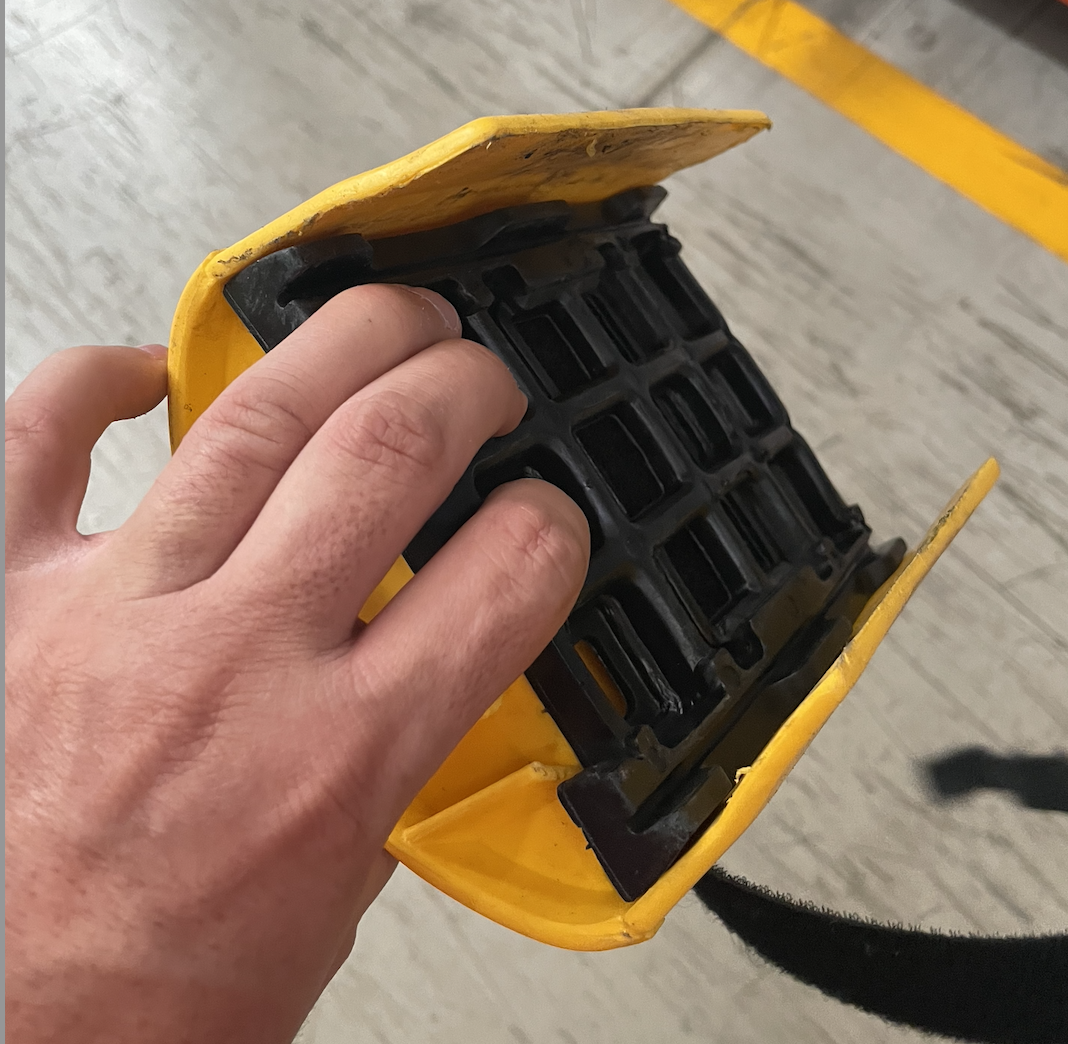 Hand holding a yellow and black grip device with a Velcro strap, used for carrying heavy items.