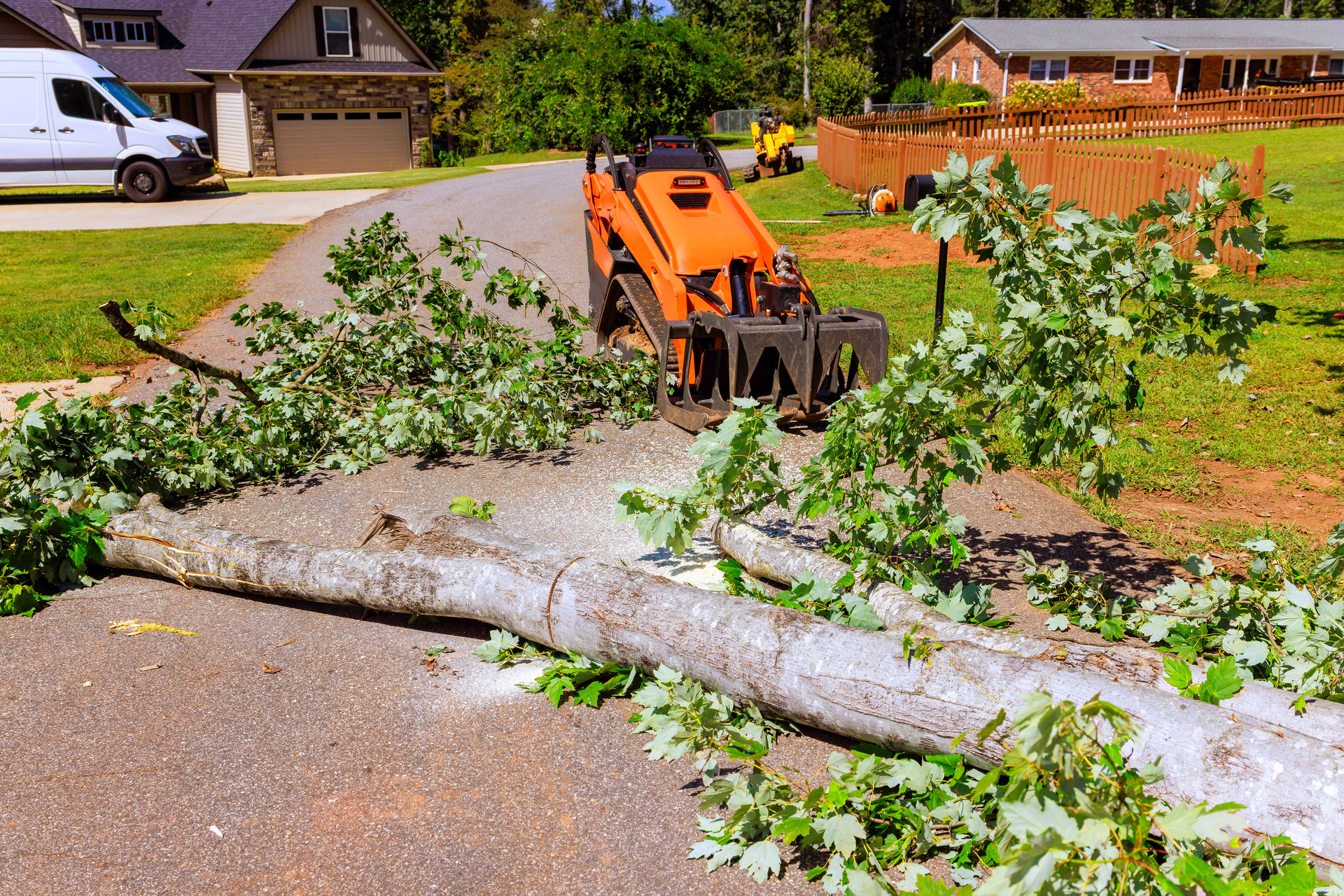 Crawler tractor loader machine removes large tree debris from road in quiet neighborhood following recent bad weather.