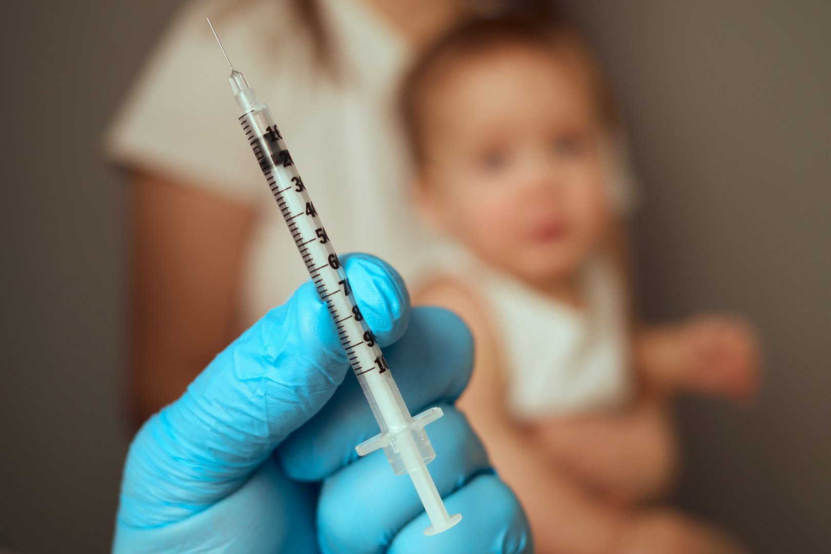 A parent holds a syringe ready for vaccination, focusing on the inoculation process. A child sits nearby, demonstrating a common healthcare practice and the importance of immunization.
