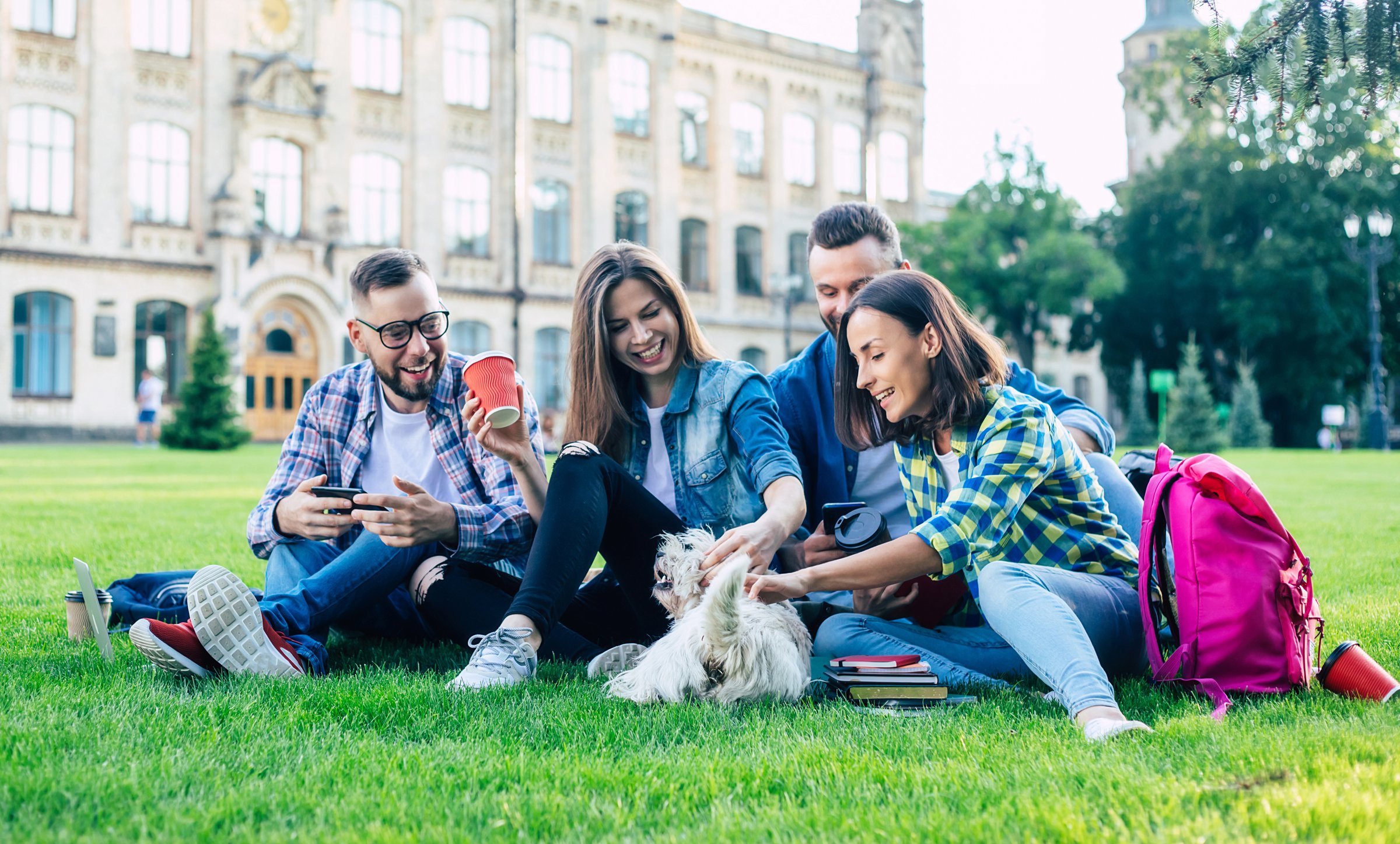 Beautiful young best friends with little funny dog on the lawn are having fun and relaxing