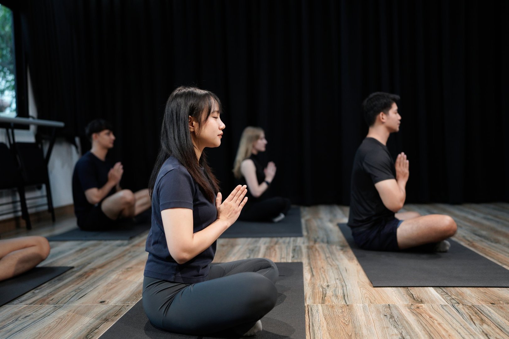 Group of young people practicing yoga In the prayer position and raised hands while sitting on mat at gym, Concept of relaxation and meditation.
