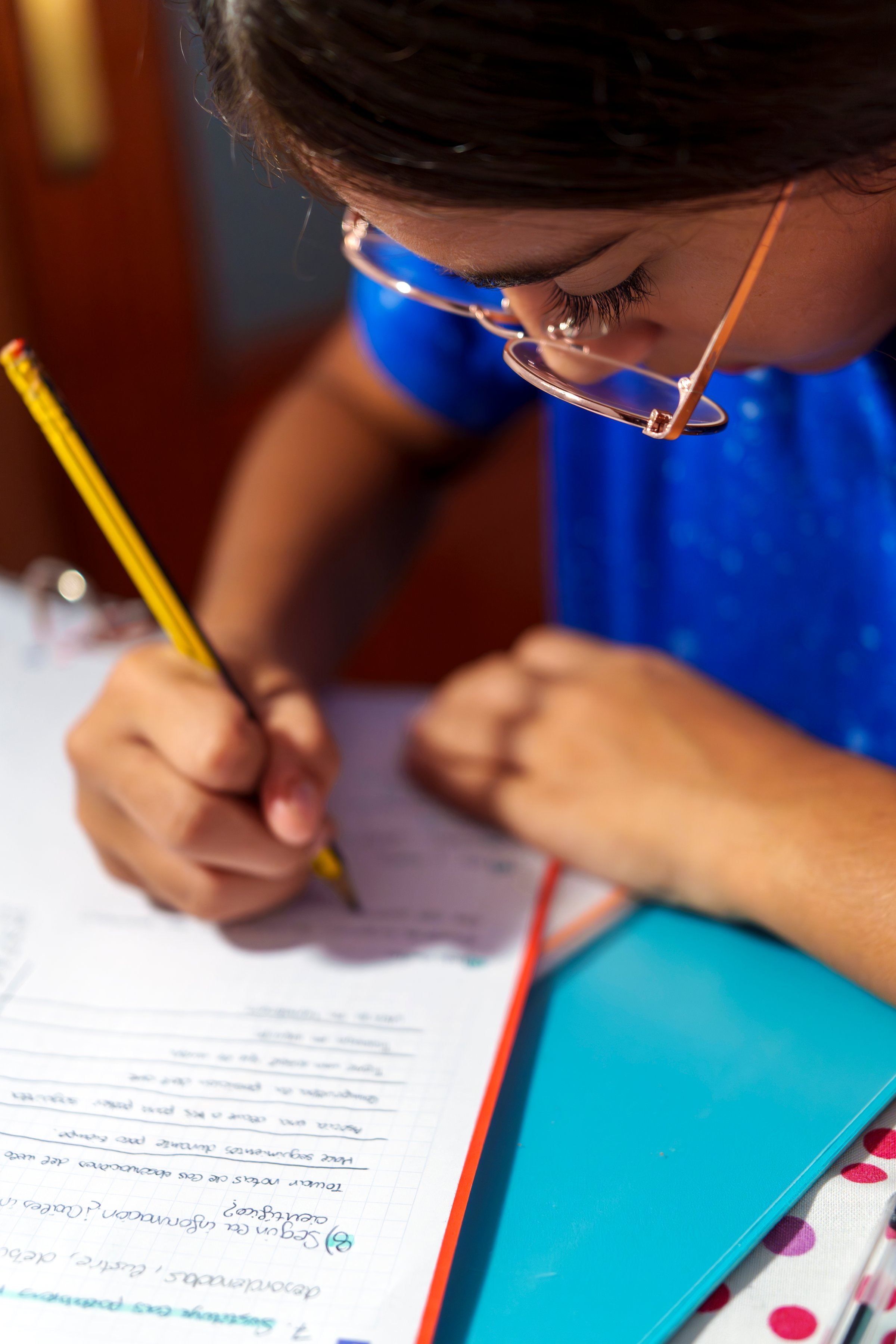 High angle close up view of teenage girl doing homework on a desk indoors wearing casual clothes.